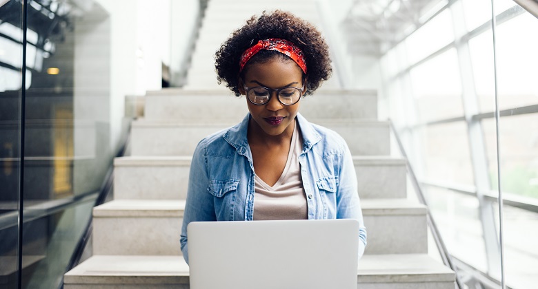 Focused young African female college student working on a laptop on some stairs on campus preparing for an exam
